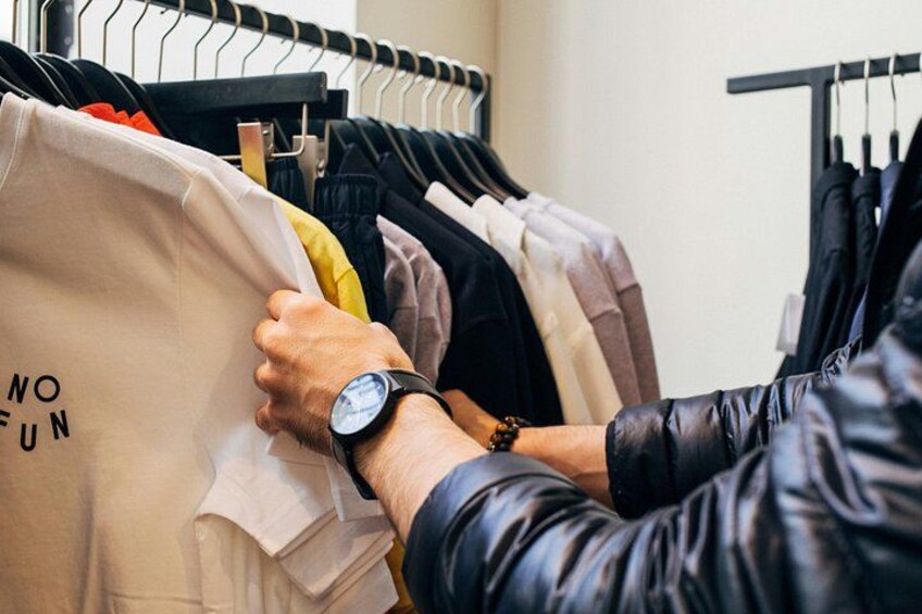 A person holding a beige bag with 'NO FUN' text, in a clothing store with various items on racks. 3
