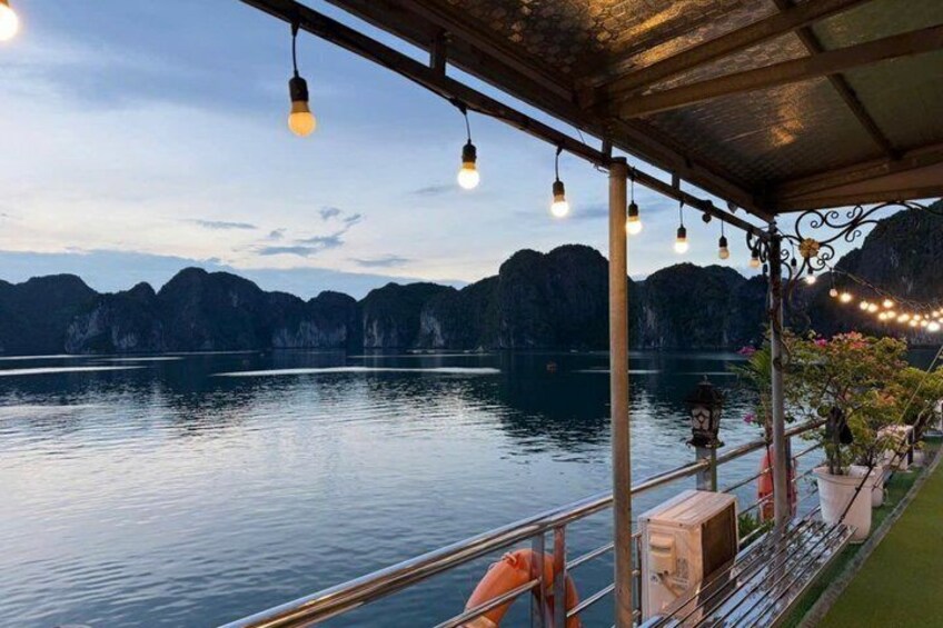 A serene lakeside view with a wooden deck, hanging lights, and distant mountains. 1