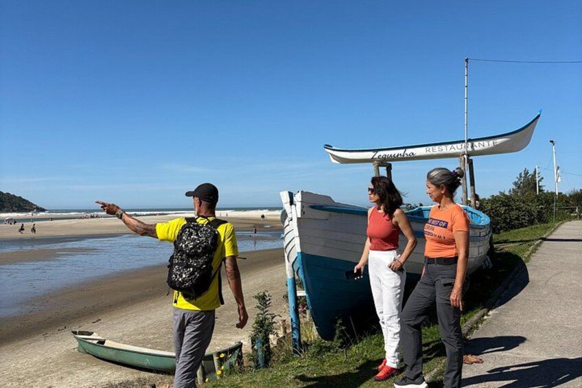 A beach with a canoe, a person pointing, and two people standing. 2
