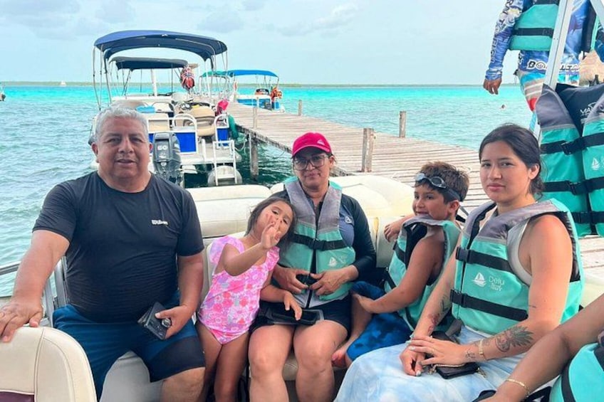 A group of people on a boat with a clear blue sea and a wooden dock in the background. 4