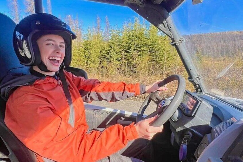A person in a red jacket driving a vehicle with a steering wheel and dashboard. 3