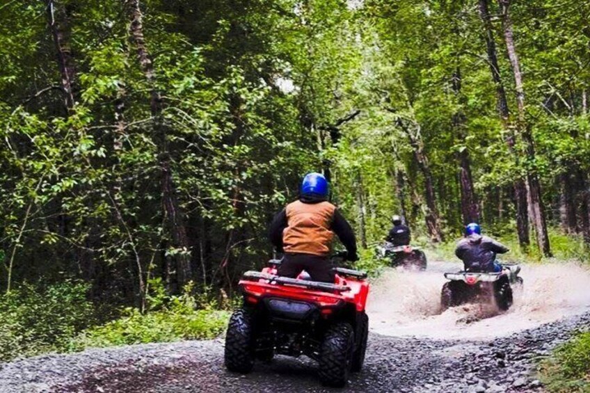 Three people riding ATVs on a gravel path through a forest. 5