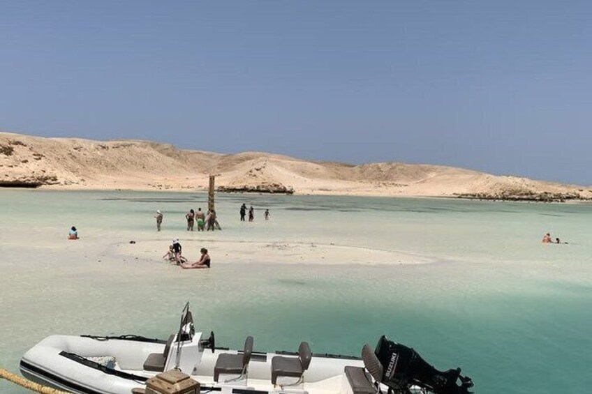 A boat on a calm beach with people swimming and sunbathing in the background. 1