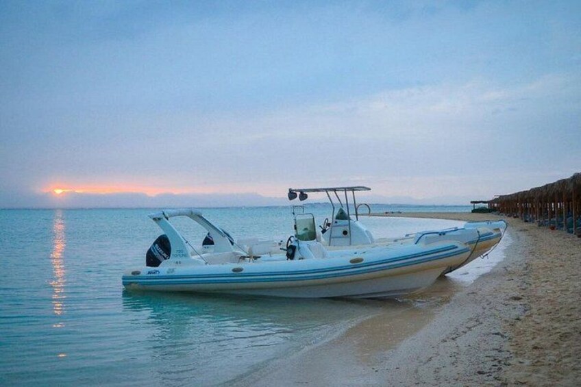 A boat on a sandy beach with calm water, a clear sky, and a sunset in the background. 4