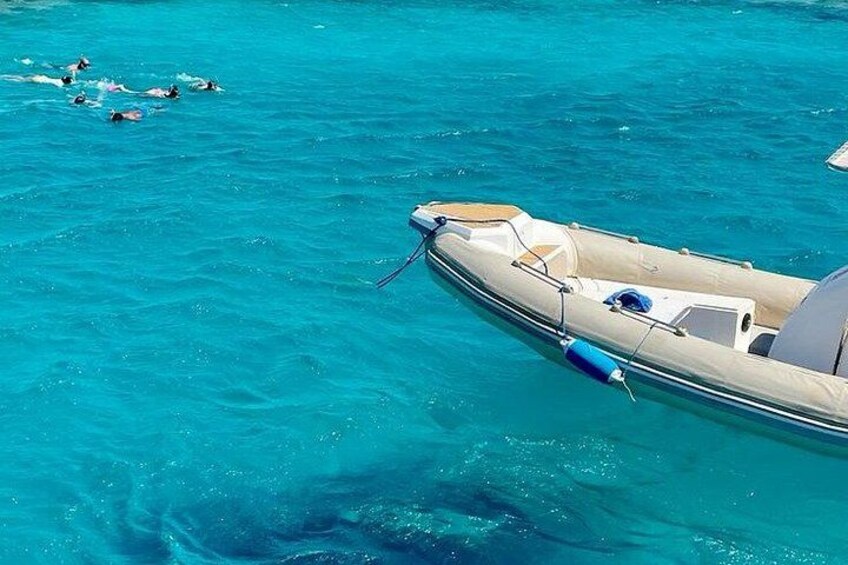 A boat anchored in clear turquoise water with swimmers in the distance. 5
