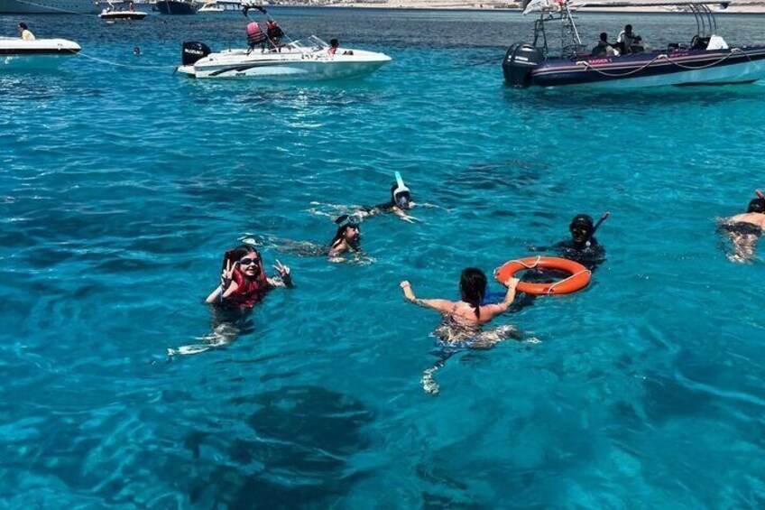 People swimming in a clear blue sea with boats in the background. 5
