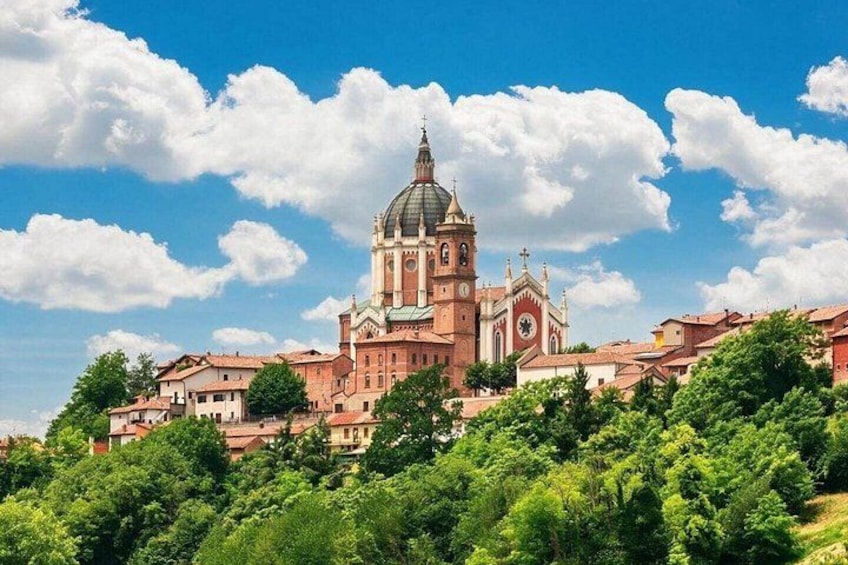 A historic church with a prominent dome and bell tower, surrounded by lush greenery and red-roofed buildings. 1