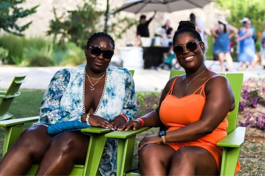 Deux personnes sont assises sur des chaises vertes à l’extérieur, avec un parc et d’autres personnes en arrière-plan. 4