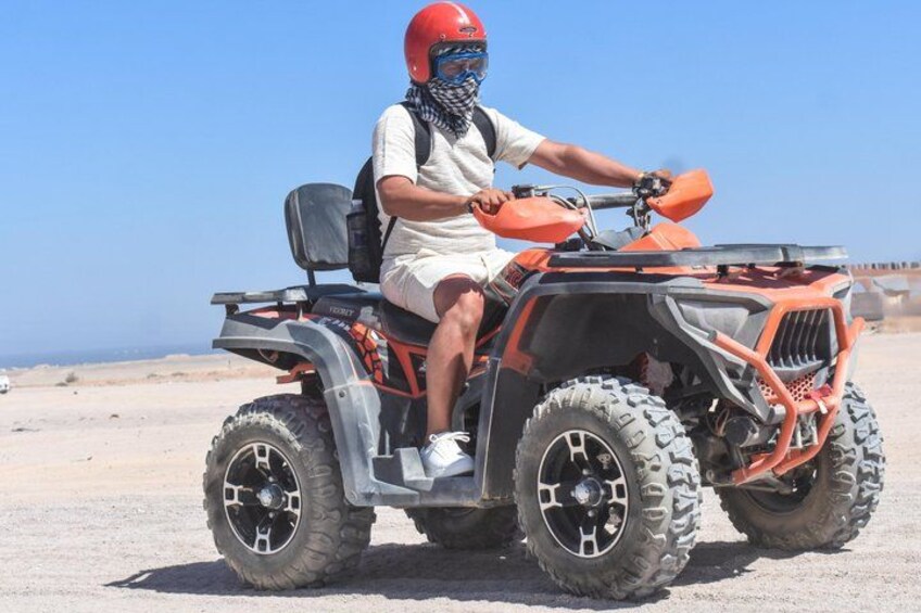 A person riding an orange ATV on a sandy terrain with a clear sky. 1