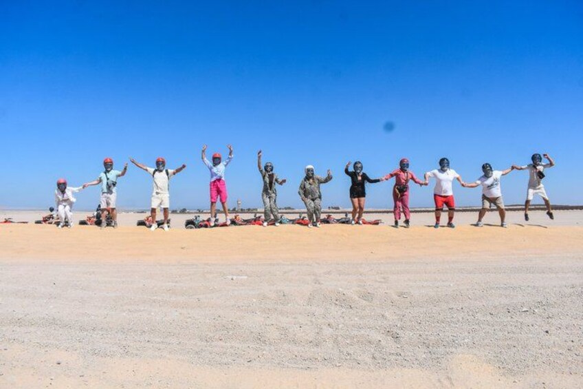 A group of people in a desert setting, some wearing helmets, with a clear blue sky in the background. 2