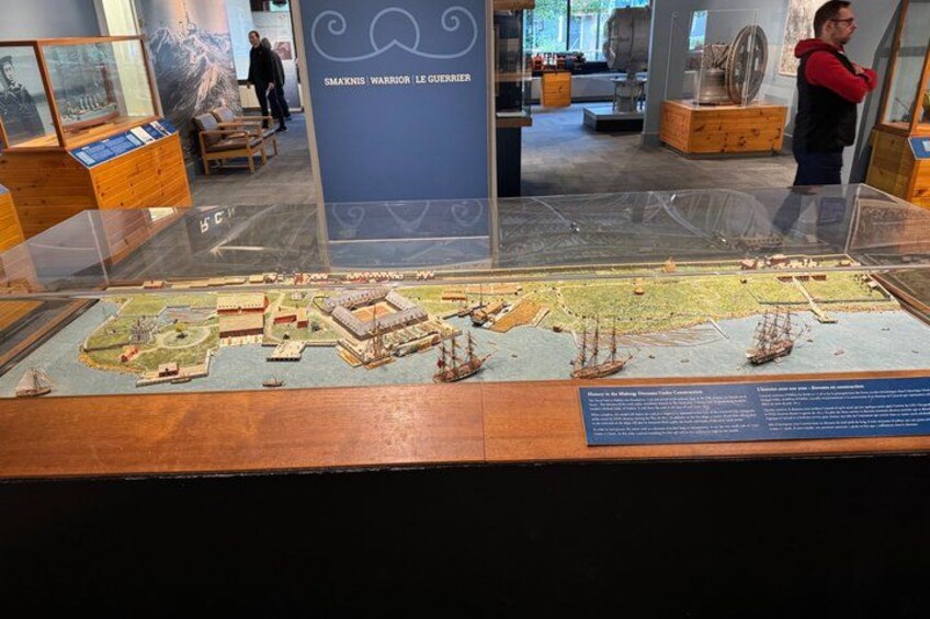 A museum exhibit with a detailed model of a historical battle scene, including ships and fortifications. 2