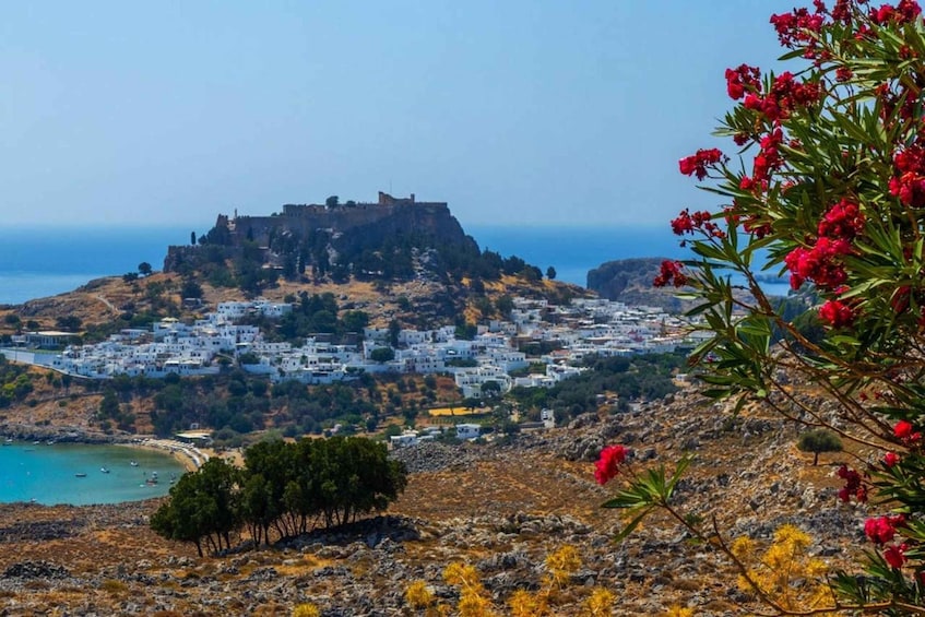 A coastal town with a historic castle on a hill, white buildings, and a clear blue sea. 2