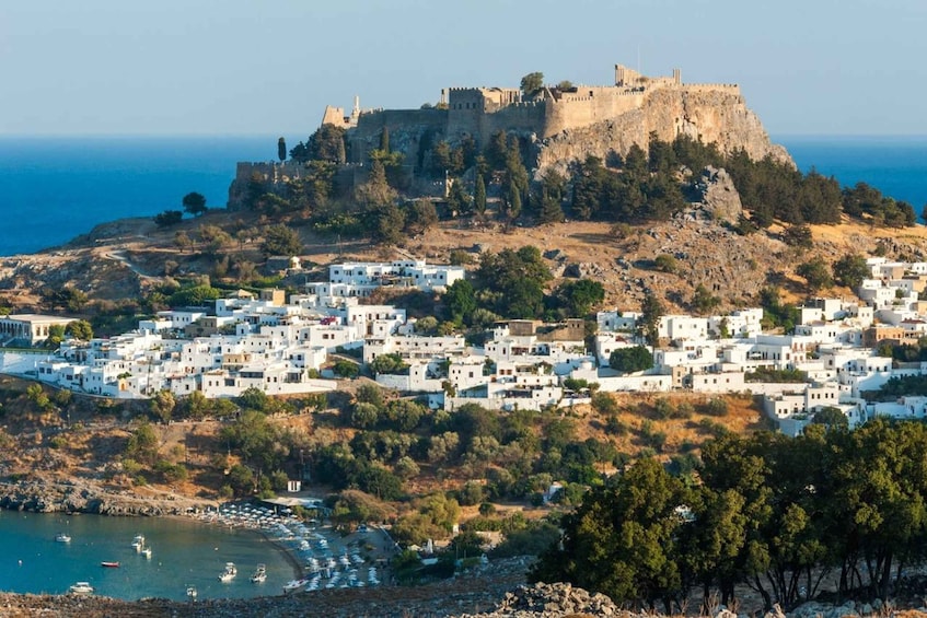 A coastal town with a prominent castle on a hill, white buildings, and a beach with boats. 4