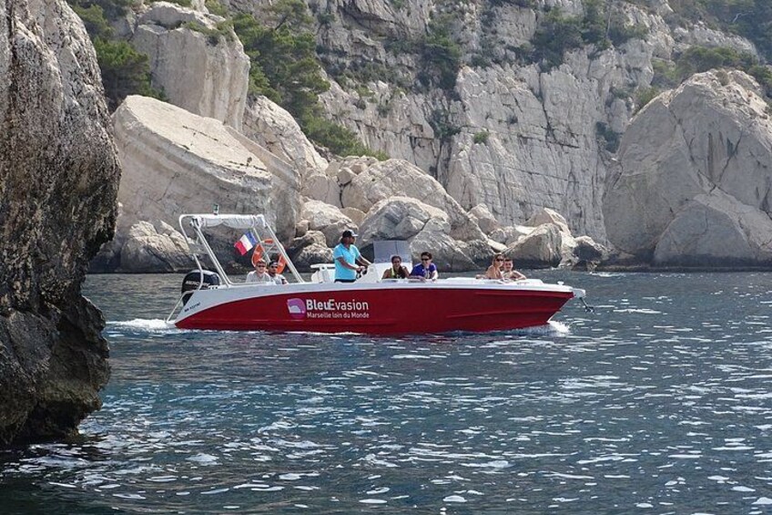 A red and white boat named 'Bleue Evasion' on water with people on board, surrounded by rocky cliffs. 4