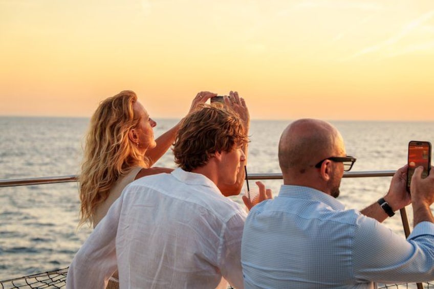 A sunset over the ocean with people taking photos. 3