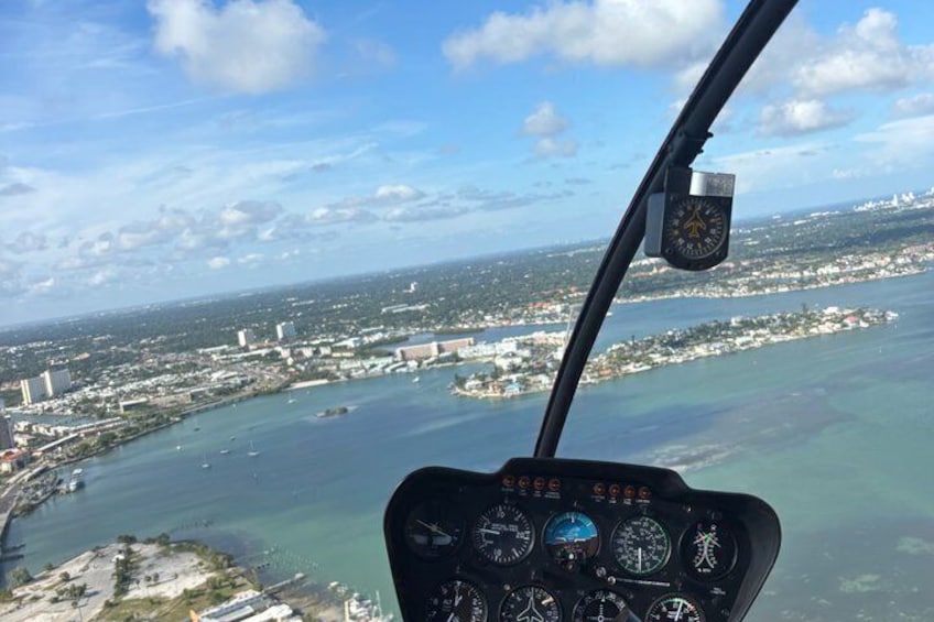 En helikoptercockpit med utsikt över en kuststad, inklusive en vik med båtar och byggnader. 3