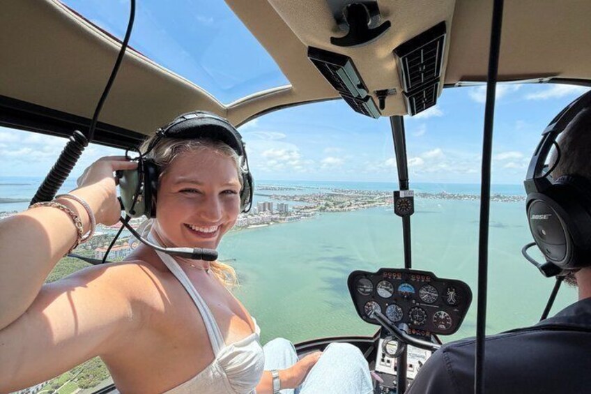 En helikoptercockpit med en person som bär ett headset, en kontrollpanel och en vy över ett kustlandskap. 1