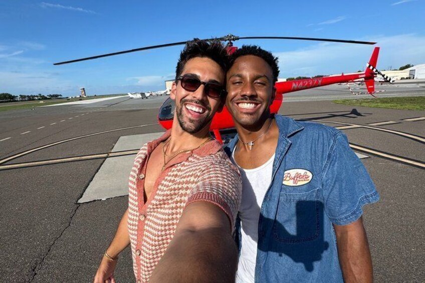 Två personer som tar en selfie med en röd helikopter i bakgrunden. 2