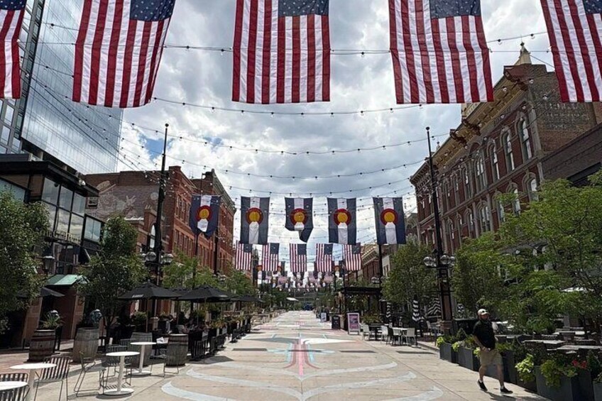 A street lined with American flags and Colorado state flags, with buildings on either side and a paved walkway in the center. 3