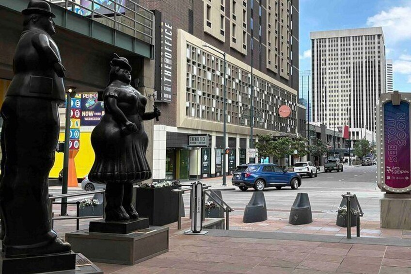 A city street with a statue of a man and woman, a tall building, and a blue car. 5