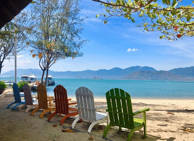 A row of Adirondack chairs on a sandy beach with a clear blue sky and mountains in the background. 2