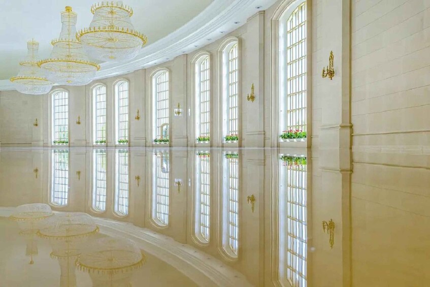 A grand hall with large arched windows, reflective floor, and ornate chandeliers. 4