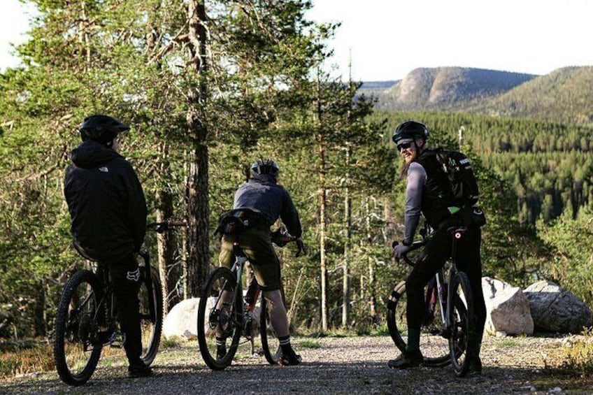 Three cyclists on a trail surrounded by trees and mountains. 1