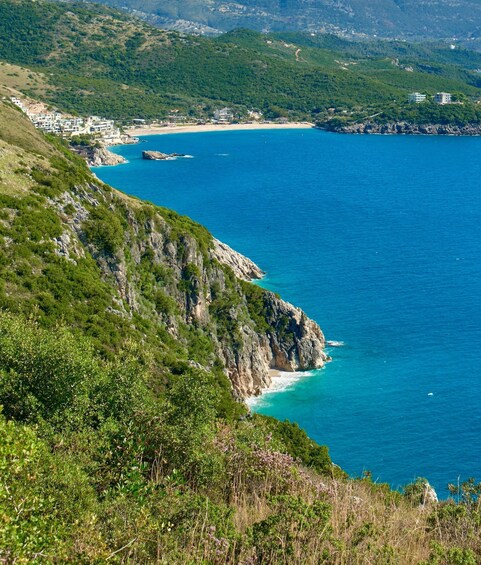 A coastal landscape with a clear blue sea, rocky cliffs, and a small town with buildings along the shore. 2