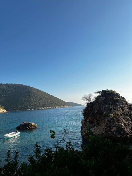 A coastal landscape with a clear blue sky, calm sea, rocky outcrops, and a boat anchored near the shore. 4