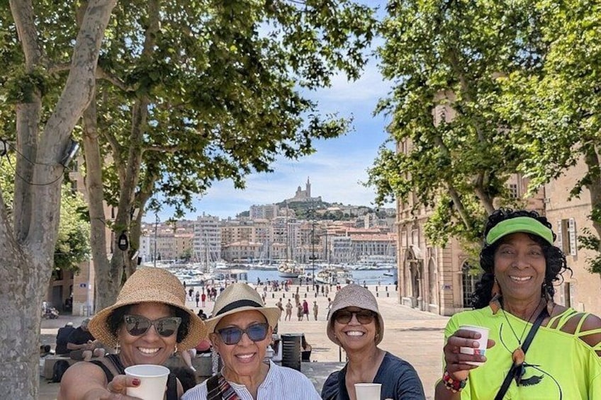 A group of people sitting on a bench, a tree-lined street, and a distant view of a harbor with boats. 1