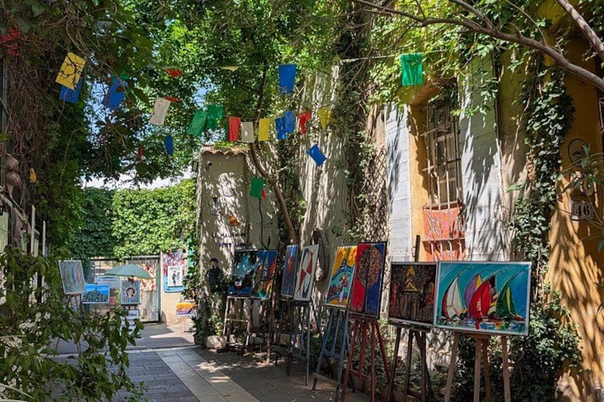 A street with art on easels, colorful flags, and buildings with vines. 3