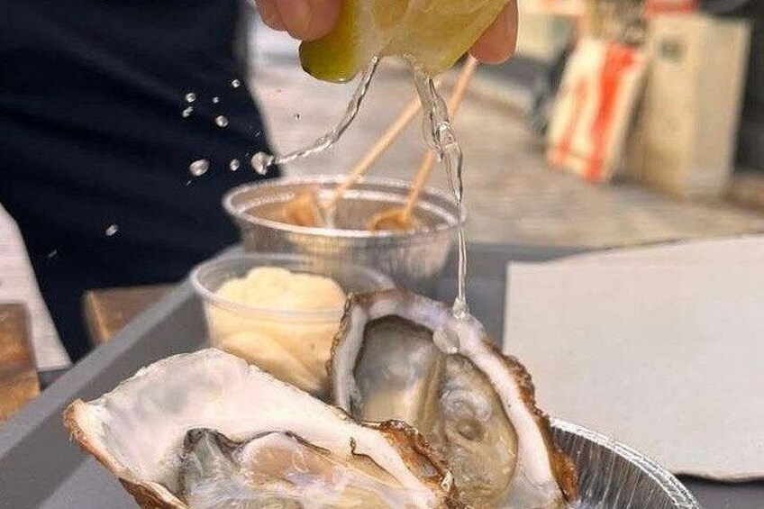 A person pouring a liquid from a squeeze bottle onto oysters in a metal tray. 5