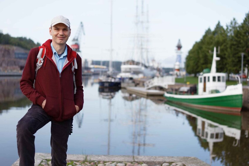 A person standing by a calm body of water with boats and a lighthouse in the background. 4