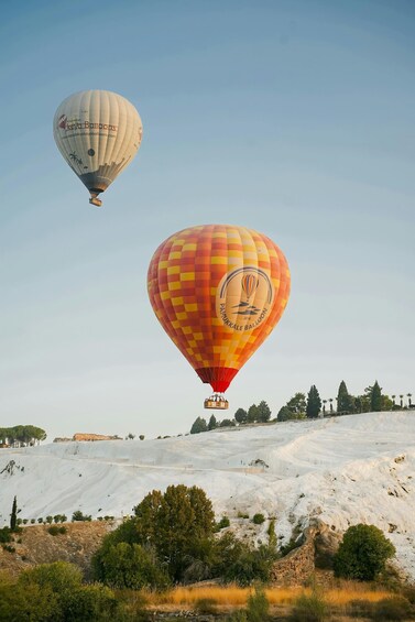Two hot air balloons flying over a hilly landscape with sparse vegetation. 3