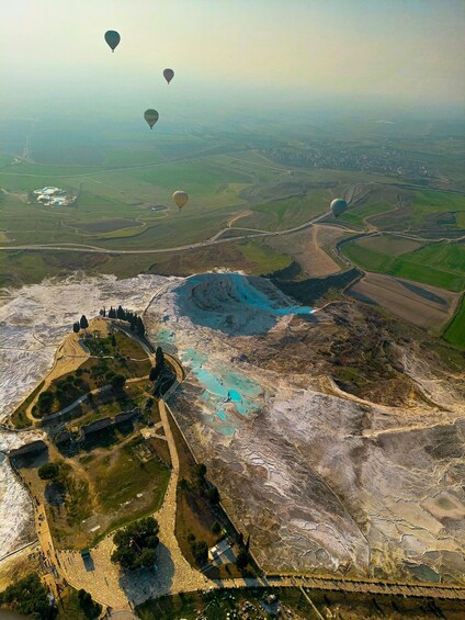 An aerial view of a landscape with terraced fields, a large body of water, and hot air balloons in the distance. 4
