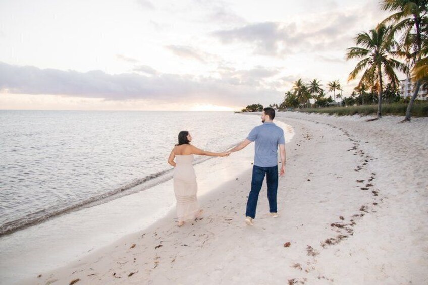 A couple walking hand in hand on a sandy beach with palm trees and a calm sea in the background. 4