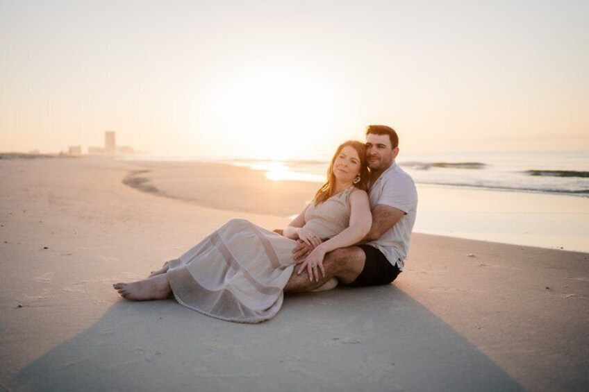 A couple sitting on a beach at sunset with the ocean in the background. 1