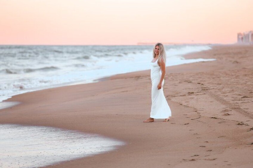 A person in a white dress standing on a beach with waves in the background. 2