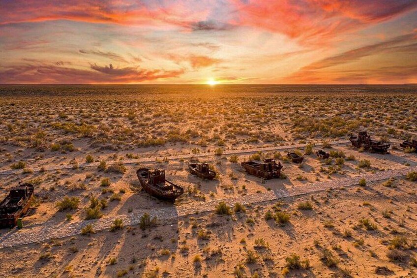A desert landscape with a sunset, sparse vegetation, and several abandoned vehicles. 5