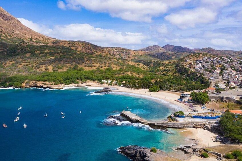 A coastal town with a beach, boats, and mountainous terrain. 1