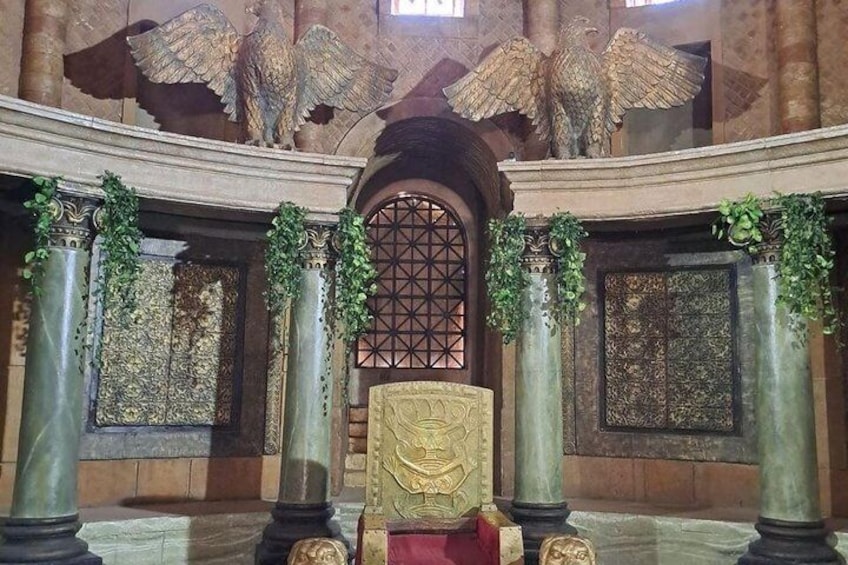 A grand hall with ornate columns, a large chair, and intricate wall decorations. 2