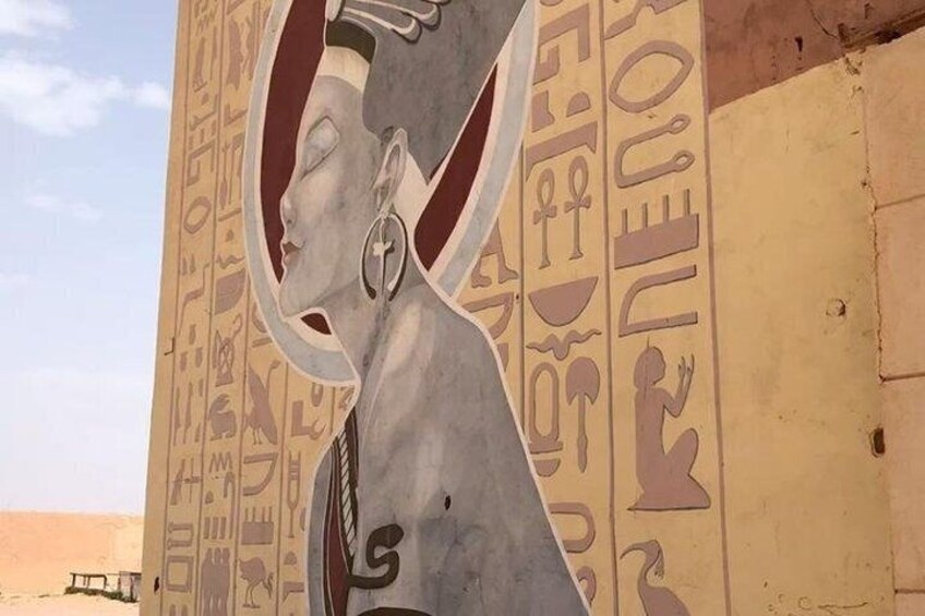 A sculpture of a woman with hieroglyphs on a wall. 4