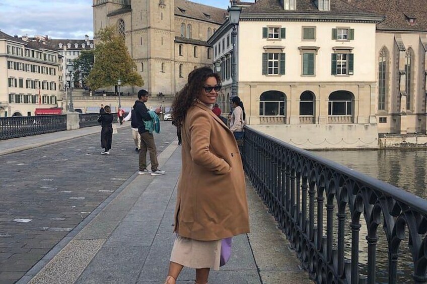 A person standing on a bridge with a river, buildings, and a railing. 1