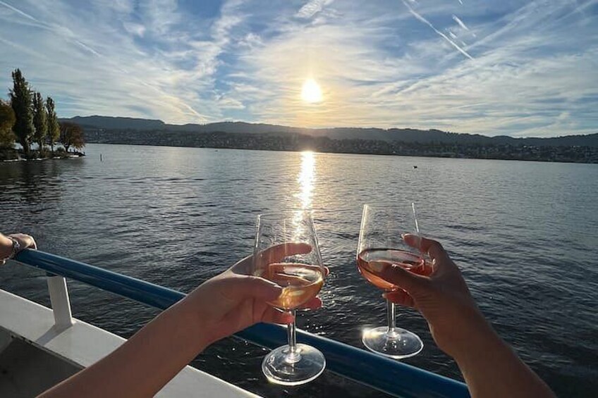 A sunset over a lake with a boat and two people holding wine glasses. 4