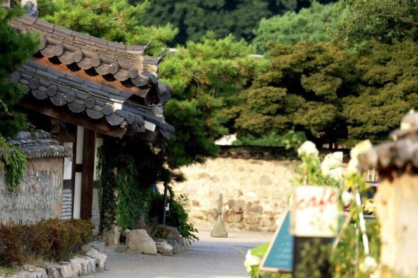 En traditionel japansk bygning med et fliset tag, omgivet af grønt og en stenvæg. 5