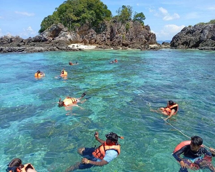 People swimming and snorkeling in clear blue water with rocky cliffs in the background. 3