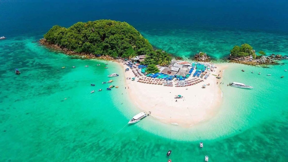 An aerial view of a tropical island with a central beach, surrounded by clear turquoise waters and lush greenery. 2