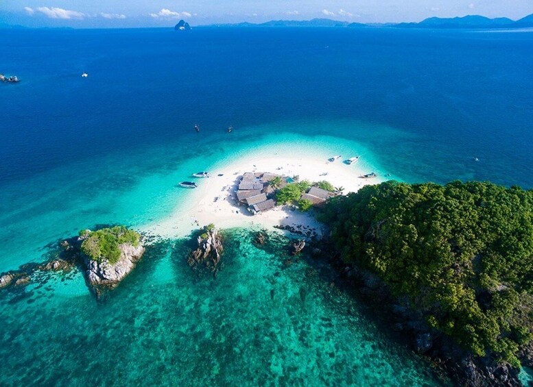 A tropical island with clear turquoise waters, a white sandy beach, and a small cluster of thatched-roof huts. 5