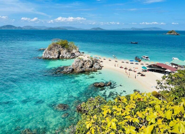 A tropical beach with clear turquoise waters, a rocky outcrop, and a small island in the distance. 1