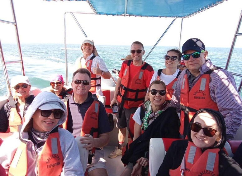 Un grupo de personas en un bote con chalecos salvavidas, y el océano al fondo. 5